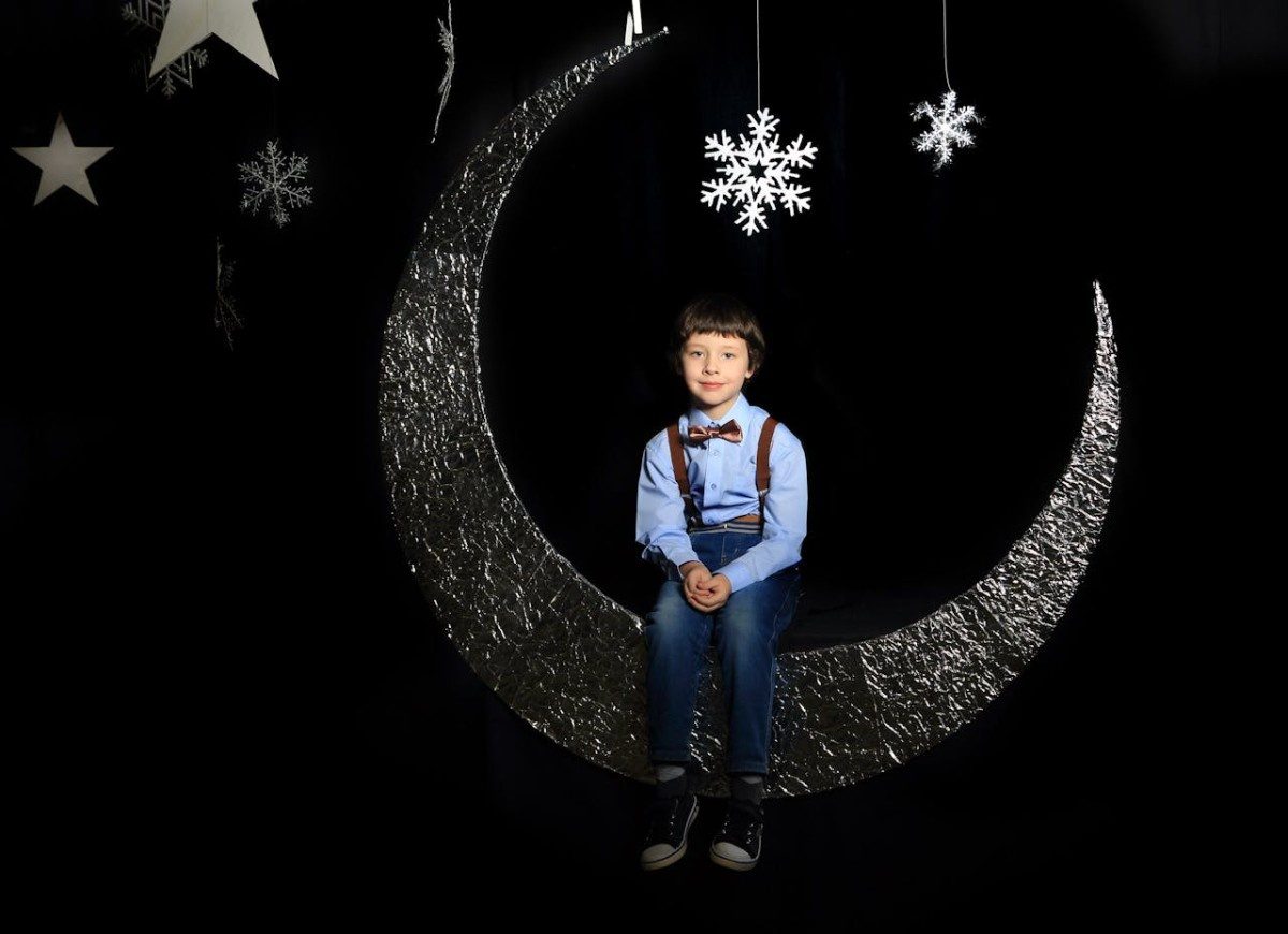 Child sitting on moon made of foil on pitch black stage