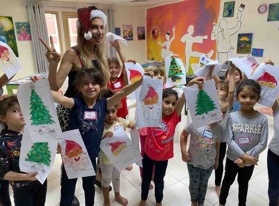 Children hold up colouring drawings with teacher wearing a Christmas hat.
