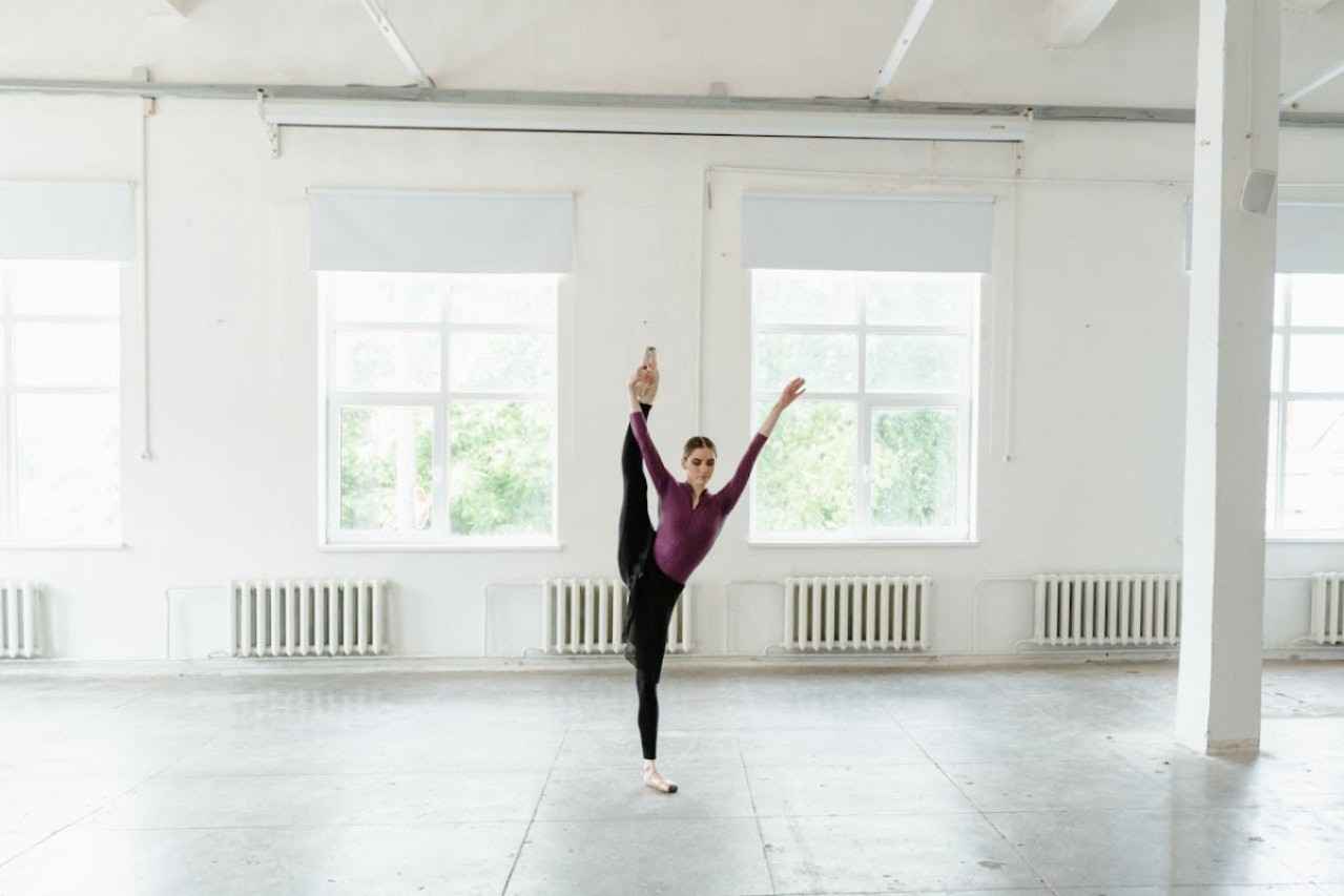 Woman in ballet studio, she is lifting one foot above her head
