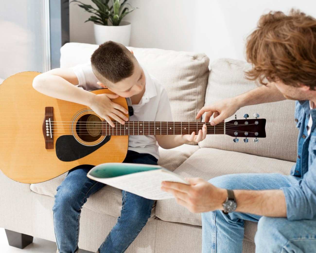 Young boy holding guitar as he is taught how to hold and play it by male instructor