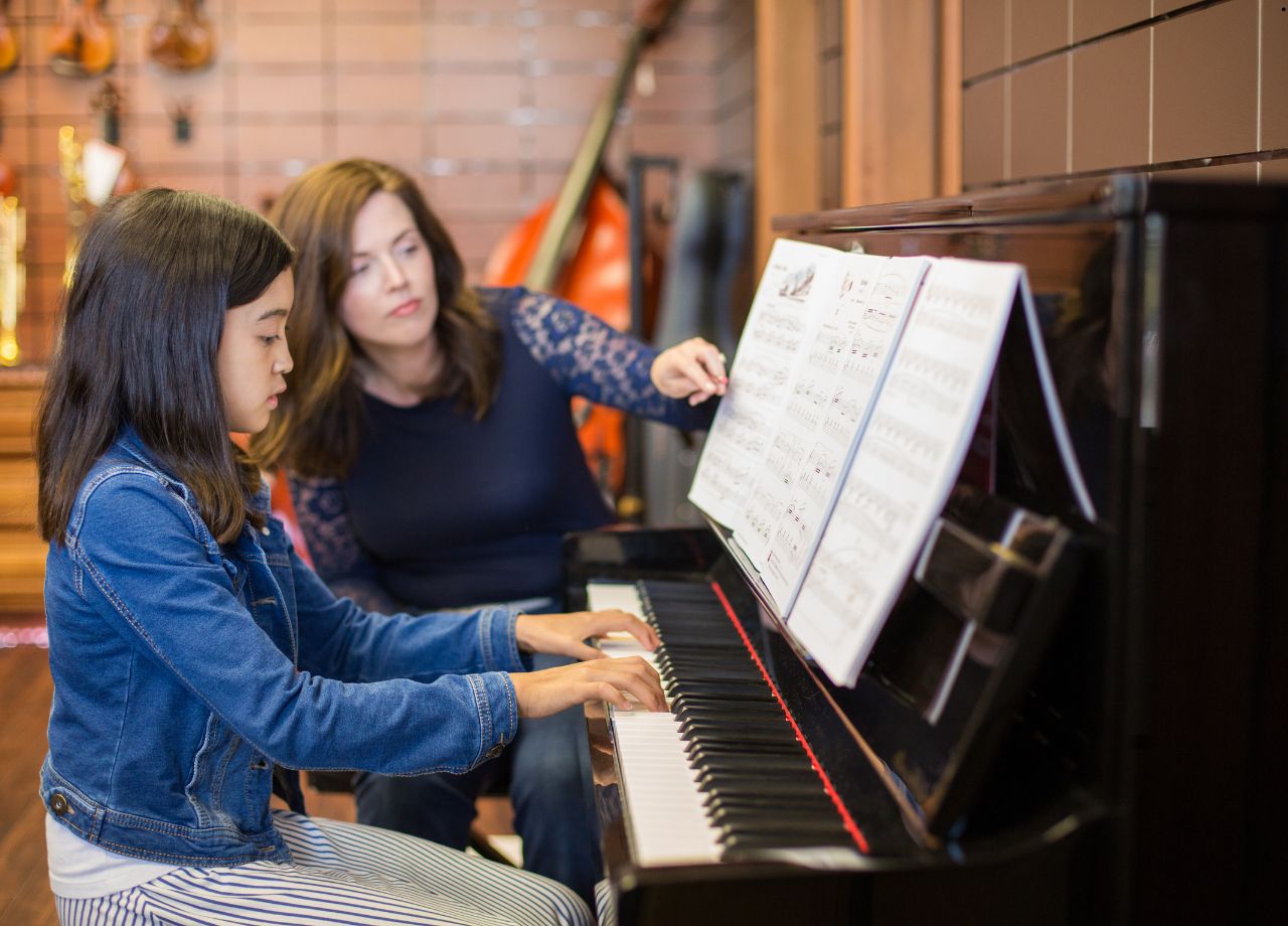 young girl being taught to play the piano by the instructor bedisde her