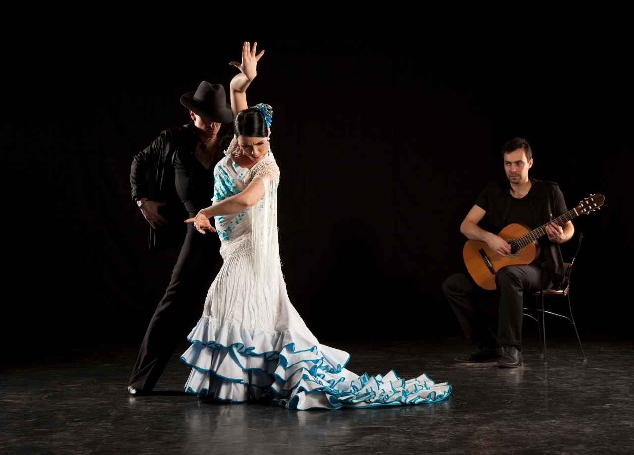 two flamenco dancers and a man sitting whilst playing the guitar.