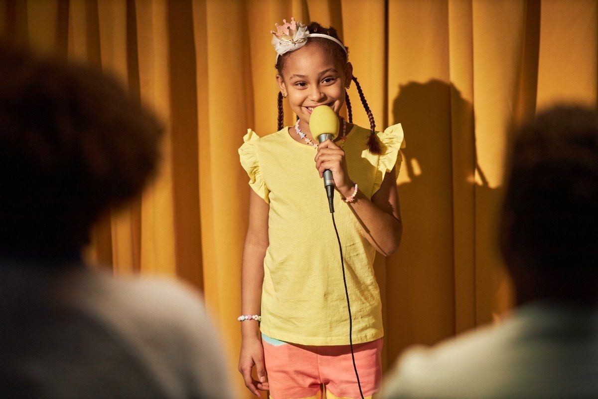 Smiling Girl Speaking To Microphone Performing for Parents