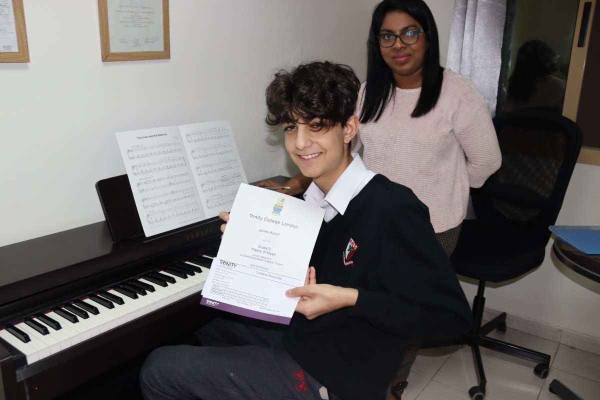 a child holding a certificate in front of a piano with teacher beside them