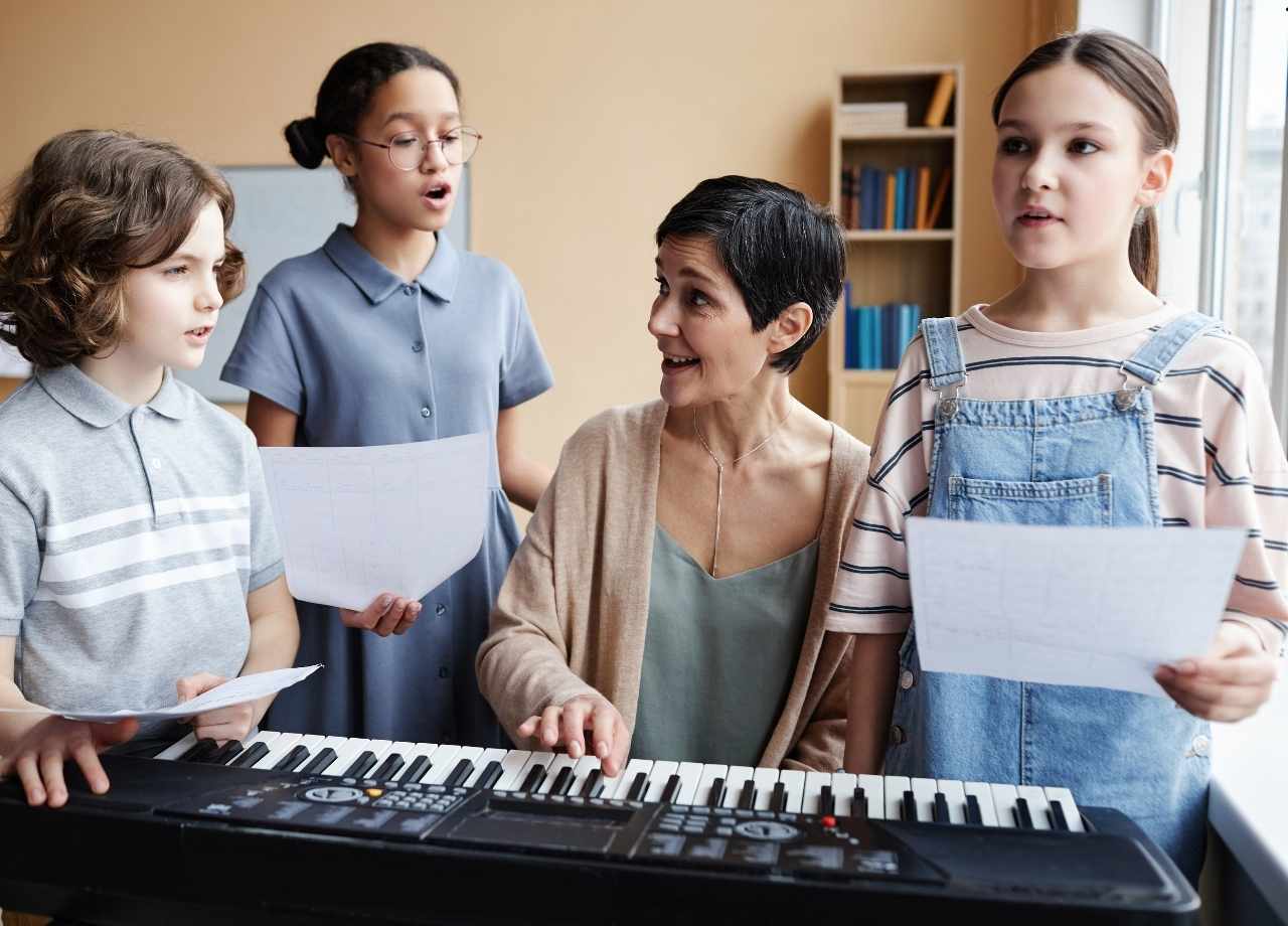 Group of you students standing around the piano teacher and singing