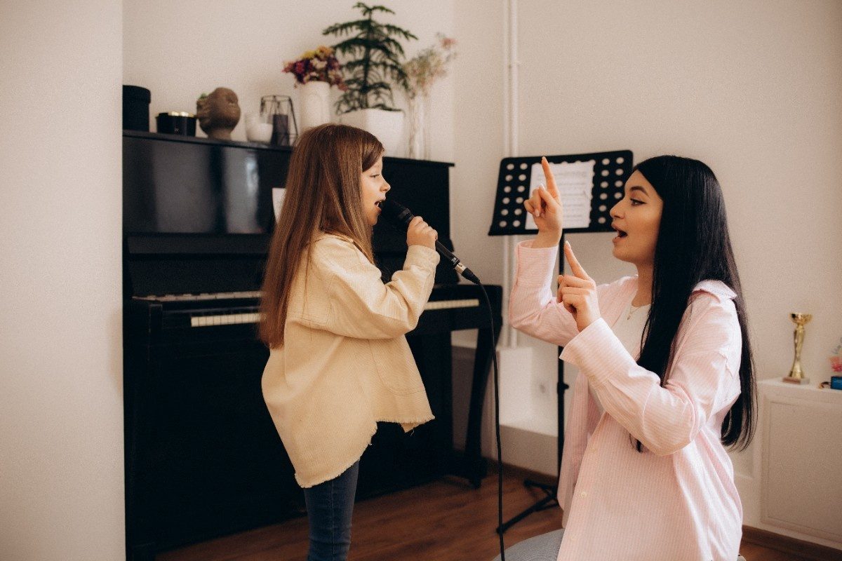 Portrait of a young girl and her mother practicing singing song during a piano lesson at home.