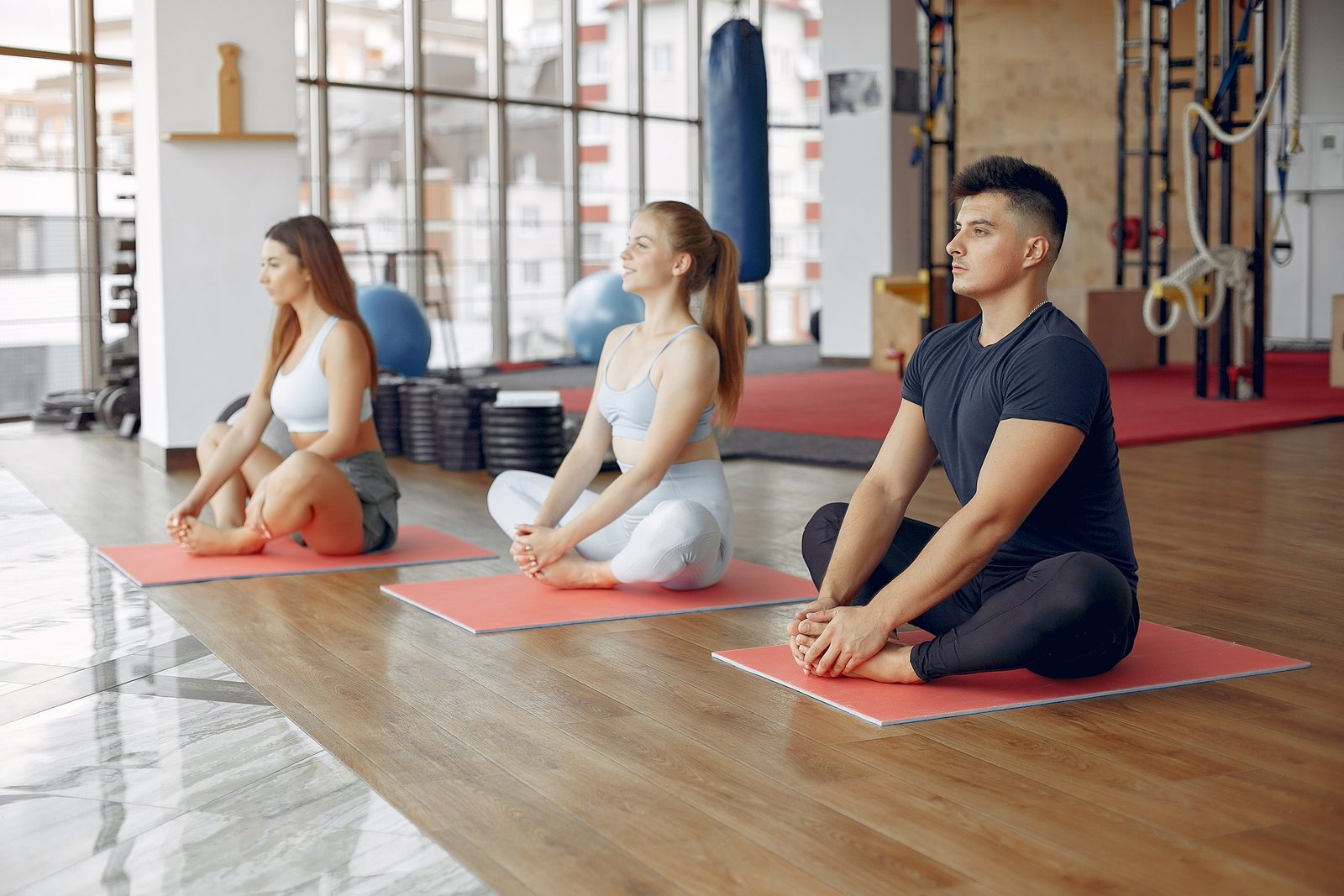 three people sitting in a gym on yoga mats