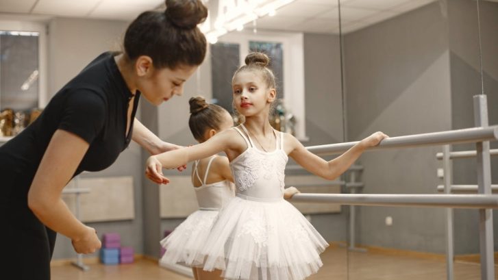Two young ballerinas being taught how to stand by instructor