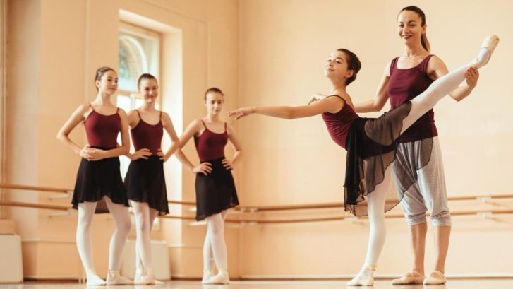 Ballerina's leg being held up in position by colleagues while three others look on
