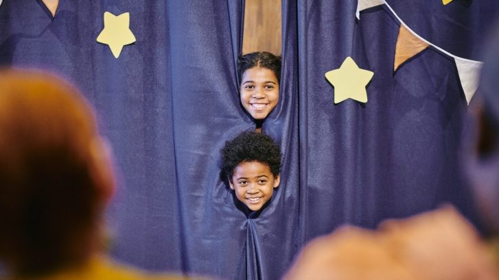 Two children peeping on stage as they get ready to perform