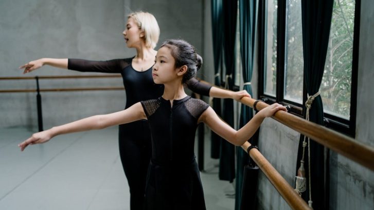 Young ballerina with trainer practicing ballet near barres
