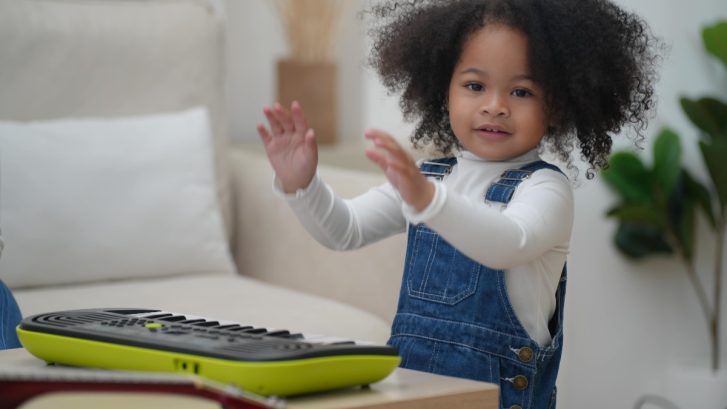young girl smiling with hands raised with a keyboard in front of her