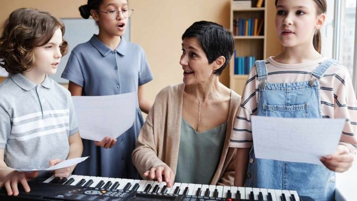 Group of you students standing around the piano teacher and singing