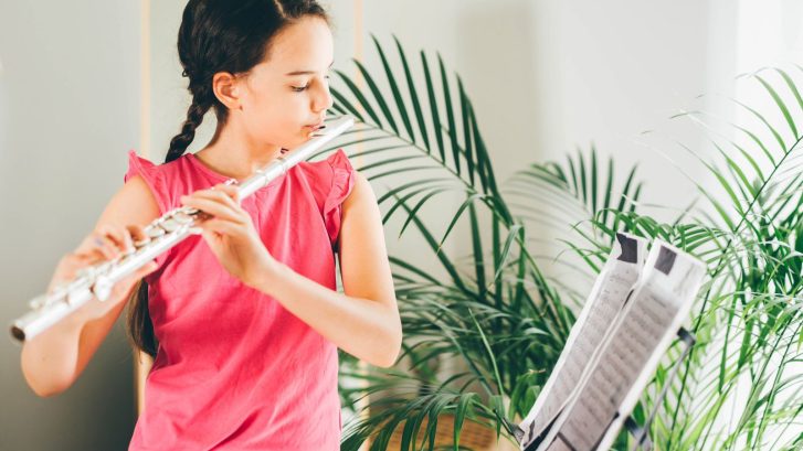 Young girl playing flute while reading music sheet