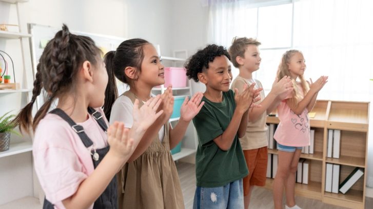 Children standing beside each other and clapping hands