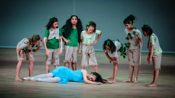 Children surrounding a fellow actress who has fallen asleep on the ground