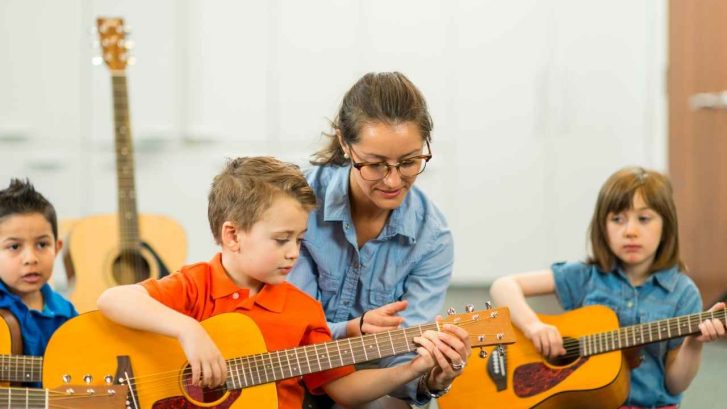 little children teaching each other to play guitar