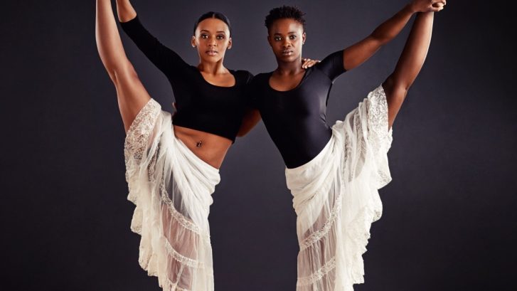 two-young-female-contemporary-dancers-holding legs up in the air