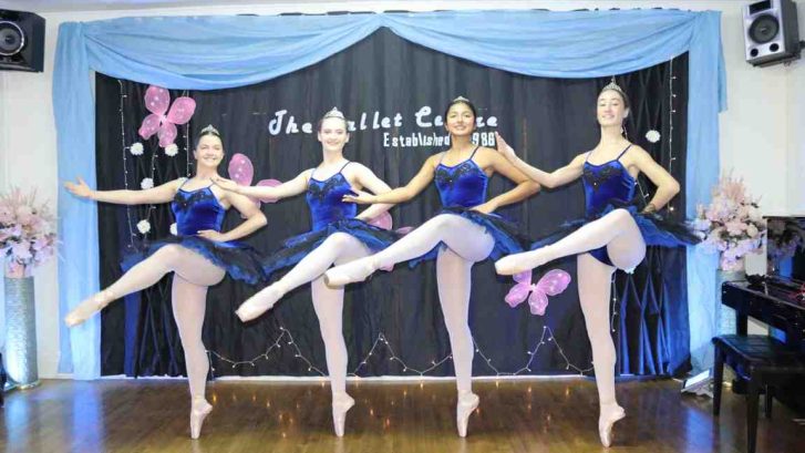 Four women wearing blue ballet attire with one leg up