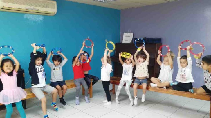 Children sitting on a bench and raising their hands above their heads