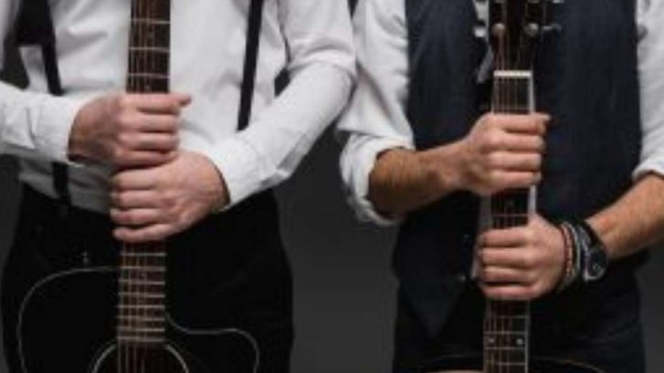 acoustic and electric guitar​ held by two men side by side