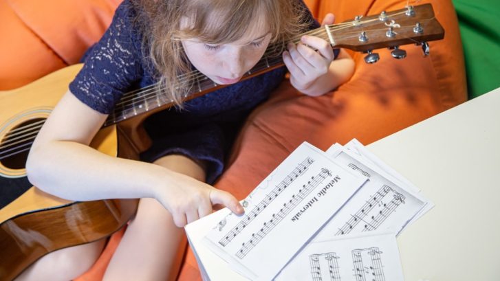 A little girl learns to play the guitar by sheet music
