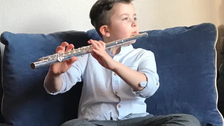 Little boy sitting on the couch and playing the flute