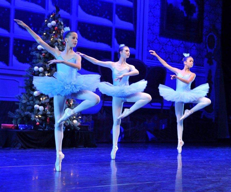three ballerinas in same pose while on stage with Christmas decorations in the background