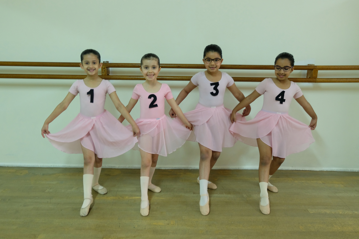 Young ballet students in pink, numbered for a graded class