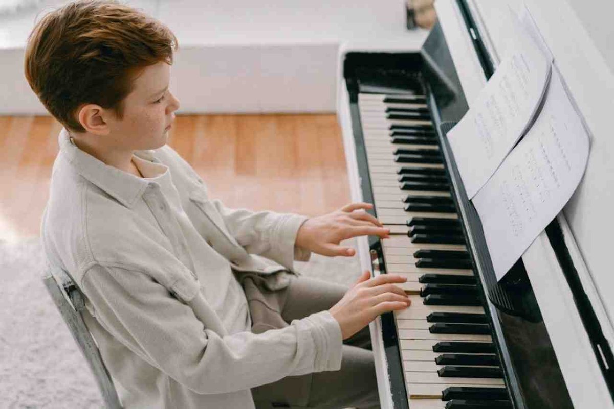 A student playing an upright piano from sheet music